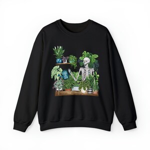 May include: Black sweatshirt with a graphic print of a skeleton watering plants. The text on the watering can says "You make me feel alive".