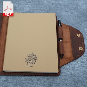 May include: A brown leather notebook cover with a pen holder and a tree design on the front. The notebook cover has a flap that closes with a snap.