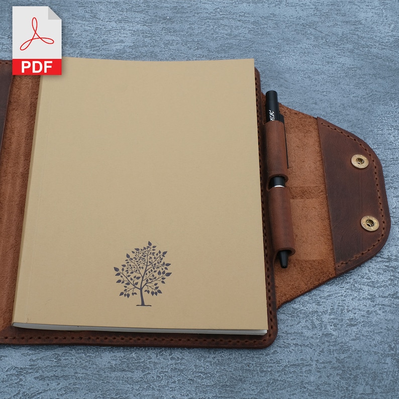 May include: A brown leather notebook cover with a pen holder and a tree design on the front. The notebook cover has a flap that closes with a snap.