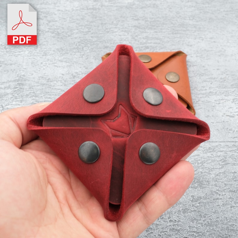 May include: A red leather coin purse with four black snaps and a red leather logo in the centre. The purse is folded closed and held in a hand.