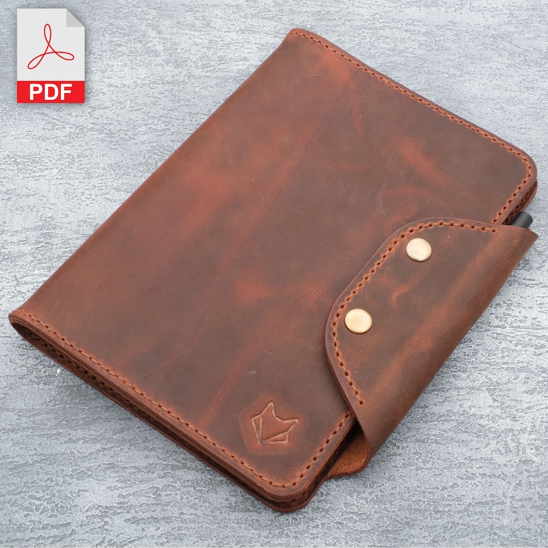 May include: A brown leather notebook cover with a pen holder and two brass snaps. The cover has a subtle distressed look and a small fox logo on the front.
