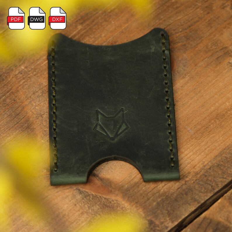 May include: A dark green leather card holder with a fox logo embossed on the front. The card holder has a stitched edge and a slot for cards.