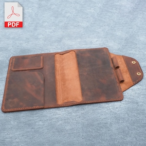 May include: A brown leather notebook cover with a flap and a pocket on the front. The cover is open to reveal a brown leather interior with a pen holder and a slot for a notebook.