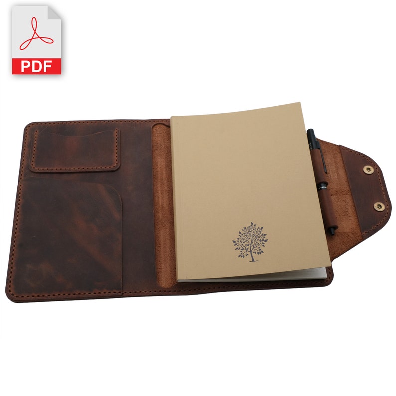 May include: A brown leather notebook cover with a pen holder and a pocket for a small notebook. The notebook cover is open to reveal a blank notebook with a tree design printed on the front.