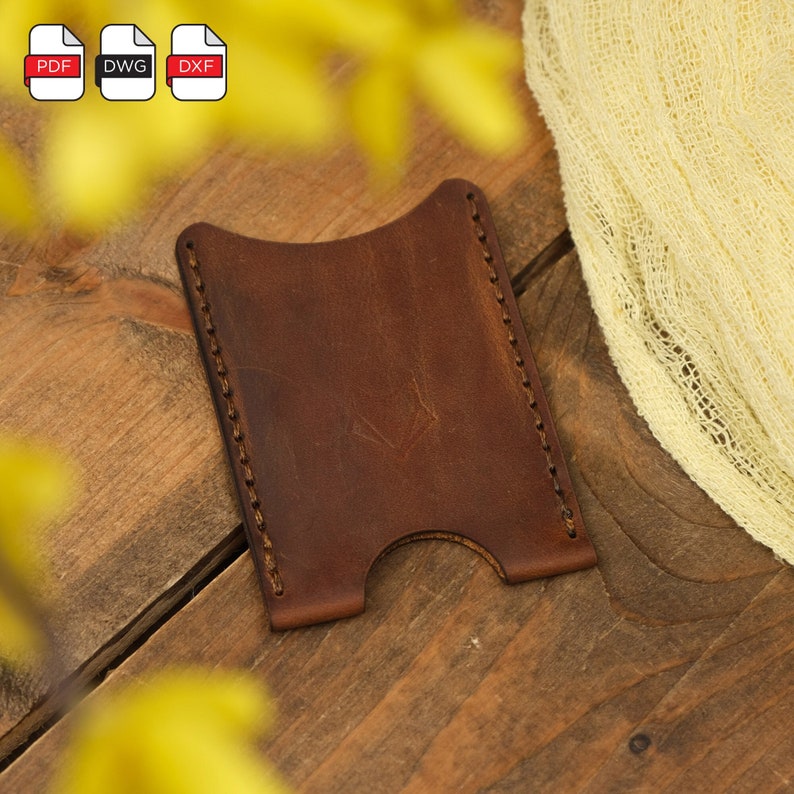 May include: A brown leather card holder with a stitched edge. The card holder is on a wooden surface.