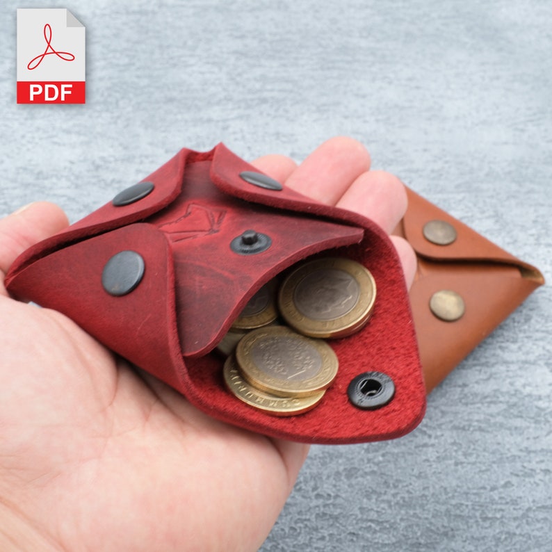 May include: A red leather coin purse with black poppers and a flap that opens to reveal a few coins. The purse is held in a hand.