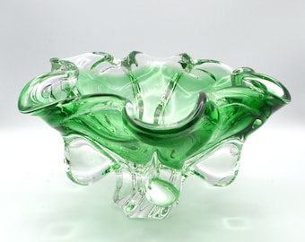 May include: A green glass bowl with a wavy, organic design. The bowl has a clear glass base with a unique, asymmetrical shape.