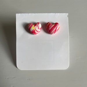 Könnte beinhalten: Ein Paar herzförmige Ohrringe mit einem marmornen Design in Pink, Weiß und Gelb.
