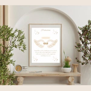 May include: A framed print with the word "Protection" at the top, featuring angel wings and the number "444". The print includes inspirational text. The artwork is displayed on a wooden bench with decorative items.