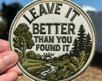 May include: Round embroidered patch with the text "LEAVE IT BETTER THAN YOU FOUND IT". The patch features a landscape design with trees, a river, and a setting sun, in shades of green and tan.