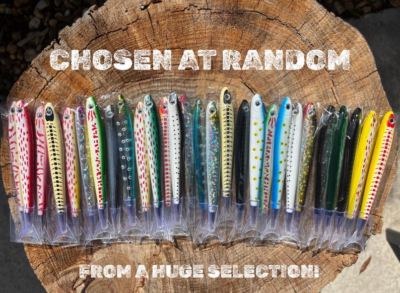 May include: A collection of fishing lures in various colors and patterns, displayed in clear plastic packaging. The lures are arranged on a wooden surface, with the text "CHOSEN AT RANDOM FROM A HUGE SELECTION!" in white.