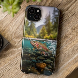 May include: A smartphone case with a colourful image of a rainbow trout in a river. The design shows the fish underwater with a forest and mountains in the background. The case has a glossy finish.