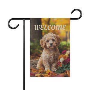 以下が含まれることがあります： 「WELCOME」の文字と、金茶色の犬の絵が描かれたガーデンフラッグ。秋をテーマにしたデザインで、カラフルな花と紅葉が描かれています。黒い金属製のスタンドに飾られています。