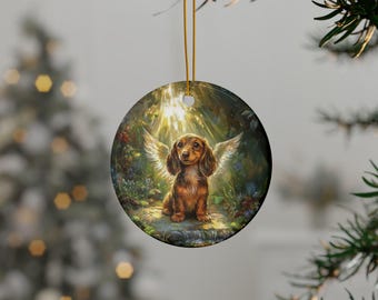May include: A round ceramic ornament featuring a brown and tan dachshund with white wings, standing in a forest setting with a golden light shining down.