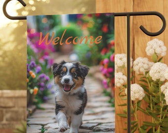 Peut inclure: Un drapeau de jardin de bienvenue avec un adorable chiot noir, brun et blanc courant sur un chemin de pierre dans un jardin avec des fleurs colorées. Le texte "Bienvenue" est écrit en orange sur le drapeau.