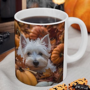 Puede incluir: Una taza de cerámica blanca con una impresión fotográfica de un West Highland White Terrier sentado entre calabazas naranjas y hojas de otoño marrones. La taza tiene un asa blanca lisa y un interior blanco, llena de una bebida oscura.