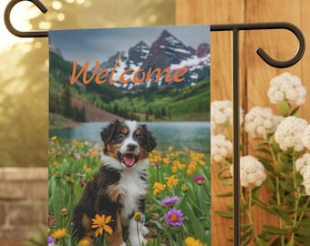 Peut inclure: Un drapeau de jardin de bienvenue avec un adorable chiot assis dans un champ de fleurs sauvages. Le drapeau présente une scène de montagne en arrière-plan et le mot "Bienvenue" en texte orange.