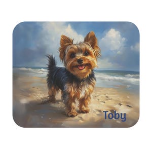 May include: A Yorkshire Terrier dog named Toby stands on a sandy beach with a blue sky and white clouds in the background.