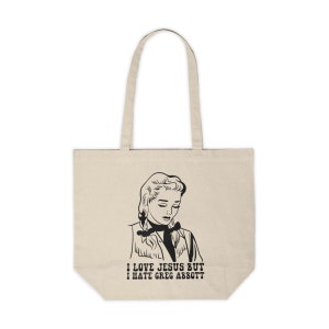 Puede incluir: Una bolsa de tela beige con una ilustración en blanco y negro de una mujer con el texto "Amo a Jesús pero odio a Greg Abbott".