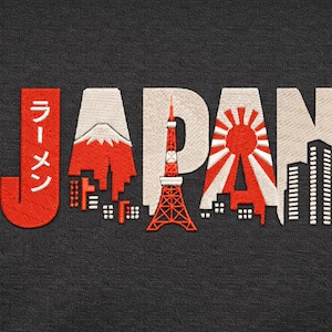 Może przedstawiać: Haftowany wzór na ciemnoszarym tle z napisem "JAPAN" z czerwonymi i białymi obrazami. Projekt zawiera górę Fuji, wieżę w Tokio i wschodzące słońce, z japońskim tekstem.