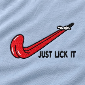 Può includere: Un tessuto azzurro con un ricamo raffigurante una lingua rossa a forma di baffo, con accenti di saliva bianca sulla parte superiore. Sotto il grafico della lingua rossa, il testo JUST LICK IT è ricamato in lettere maiuscole nere.