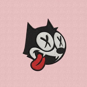 Puede incluir: Parche bordado con la cabeza de un gato negro con ojos blancos tachados con una X, una boca blanca y una lengua roja. Sobre un fondo rosa claro.