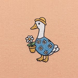 May include: An embroidered patch featuring a charming goose wearing a yellow hat and a blue dress adorned with white flower details. The goose is holding a potted flower, set against a peach-colored background.