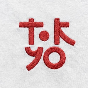 May include: A close-up of white fabric featuring the embroidered word "TOKYO" in red Japanese characters. The design is bold, with a textured, stitched appearance, creating a striking visual effect.