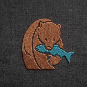 May include: Embroidered patch showing a brown bear with a blue fish in its mouth. The bear is in a cartoon style. The patch is on a dark grey fabric background.