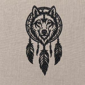 May include: A black machine embroidery design featuring a wolf head centred within a circular dreamcatcher frame. The design includes three hanging feathers suspended from the circular frame by thin lines with small circular beads.