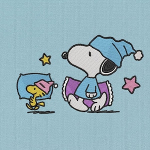 Może przedstawiać: Haftowany wzór przedstawiający Snoopy'ego i Woodstocka w piżamach i czapkach nocnych, otoczonych gwiazdami. Snoopy siedzi, a Woodstock leży na poduszce. Wzór znajduje się na jasnoniebieskim tle.