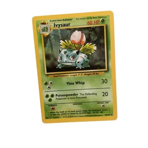 May include: A Pokémon trading card featuring Ivysaur, a Stage 1 Pokémon. The card has a green and yellow border with the text "Ivysaur" and "60 HP." The card also includes the text "Vine Whip" and "Poisonpowder." The card measures 99 cm in length and weighs 13 kg.