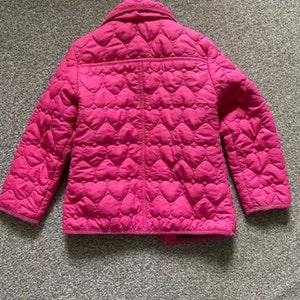 May include: A pink quilted jacket with a heart pattern. The jacket has a zipper closure and a collar.