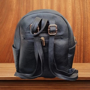 May include: A black leather backpack with gold buckles and zippers. The backpack has a rounded shape and adjustable straps.