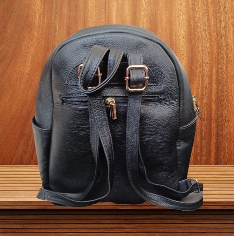 May include: A black leather backpack with gold buckles and zippers. The backpack has a rounded shape and adjustable straps.