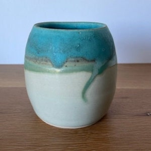May include: A white ceramic vase with a teal glaze. The glaze has a drip effect, creating a unique and artistic look.