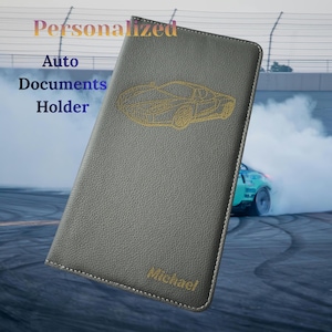 May include: Gray leather auto documents holder with a gold car outline. The holder has the word "Personalized" at the top, "Auto Documents Holder" on the left, and the name "Michael" at the bottom.