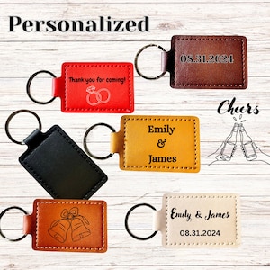May include: A collection of rectangular leather keychains in red, dark brown, black, yellow, tan, and cream. The keychains feature engraved text including 'Thank you for coming!', 'Emily & James', and '08.31.2024', along with icons of wedding rings and bells.