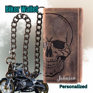 May include: Brown leather biker wallet with a skull design and a chain. The wallet has the name "Johnson" and the word "Personalized" printed on it. The words "Biker Wallet" are printed at the top of the image. A motorcycle is in the background.