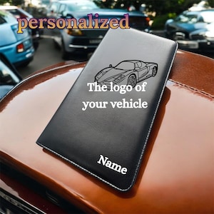 May include: Black leather wallet featuring a car logo, the text "The logo of your vehicle" and "Name". The word "personalized" is in the background. The wallet is on a brown surface.