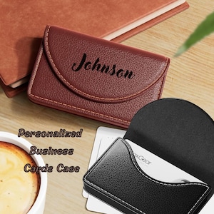 May include: A burgundy leather business card case with the name "Johnson" embossed on the front. The case is open, revealing white business cards. The text "Personalized Business Cards Case" is also visible.