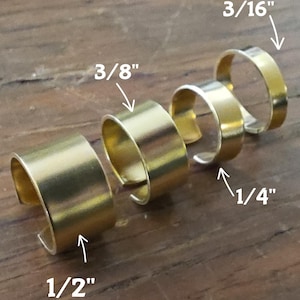 May include: Four gold-colored ear cuffs of varying sizes, arranged on a wooden surface. The sizes are labeled as 1/2", 3/8", 1/4", and 3/16", showcasing the range of available options. The cuffs have a simple, minimalist design.