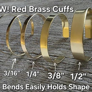 May include: Several gold-colored brass cuffs of varying widths are displayed, ranging from 1/8" to 1/2". The text "NEW! Red Brass Cuffs" and "Bends Easily Holds Shape" are visible. The cuffs are arranged on a wooden surface.