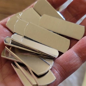 May include: A stack of silver-colored metal blanks, each with a rounded edge. The blanks are arranged in a fan shape, with the top blank partially covering the ones below.