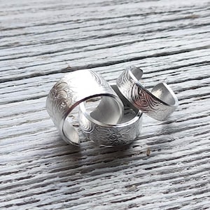 May include: Three silver rings with a floral design. The rings are stacked on top of each other.