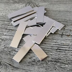 May include: A pile of silver-colored metal rectangles, likely for crafting or jewelry making.