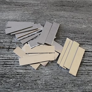 Puede incluir: Una pila de tiras de metal plateadas, algunas están apiladas unas sobre otras, sobre una superficie de madera.