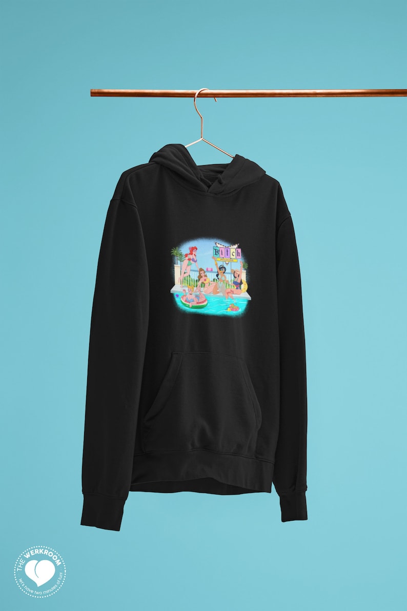 Może przedstawiać: Czarna bluza z kapturem z przednią kieszenią i kolorową grafiką. Grafika przedstawia scenę przy basenie z postaciami, basenem i napisem "Bitch". Bluza wisi na miedzianym pręcie na niebieskim tle.