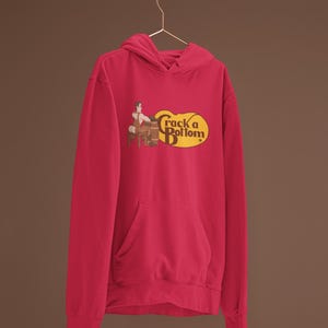 May include: A red hoodie with a front pocket and a drawstring hood. The hoodie features a graphic with the text "Crack a Bottom" in a yellow oval, with a cartoon image of a person sitting on a barrel.