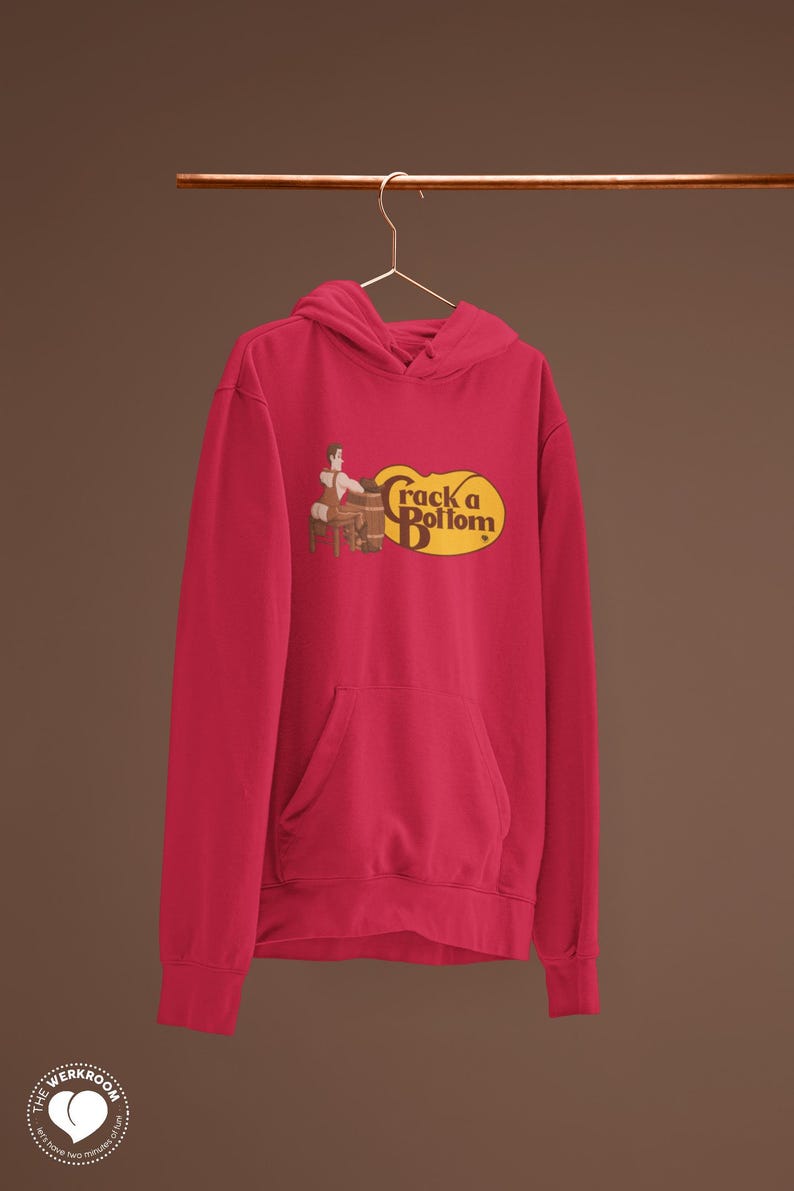 May include: A red hoodie with a front pocket and a drawstring hood. The hoodie features a graphic with the text "Crack a Bottom" in a yellow oval, with a cartoon image of a person sitting on a barrel.